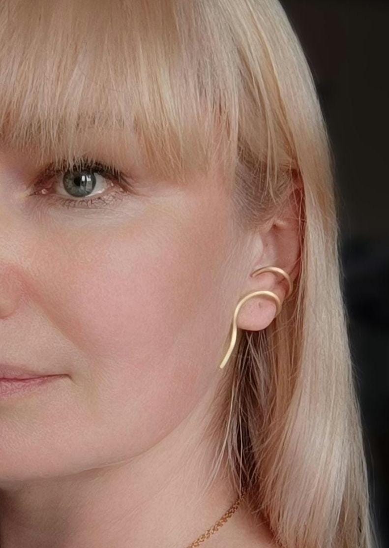 Minimalist brass ear cuff worn on ear – modern curved unisex jewelry piece in matte gold finish